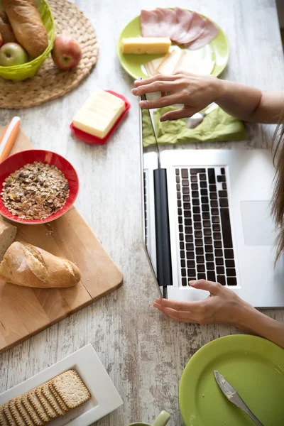 ラップトップ コンピューターを使用しながら朝食を持つ若い女性 — ストック写真