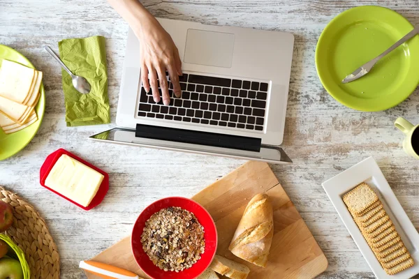 Ung kvinna äter frukost medan du använder en bärbar dator — Stockfoto