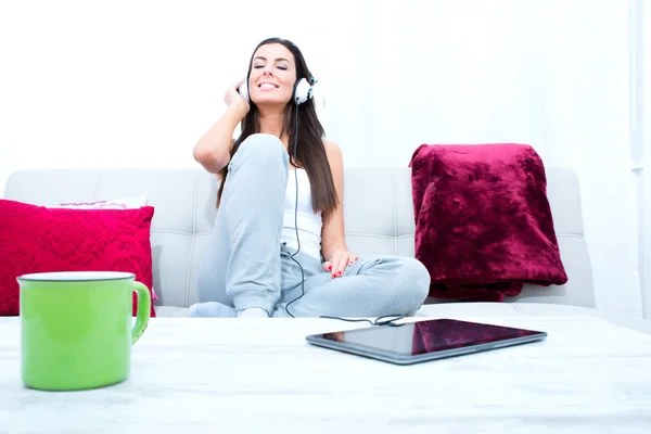 Joven hermosa mujer escuchando música con un Tablet PC en hom —  Fotos de Stock