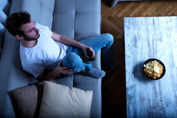 Joven viendo televisión por la noche con papas fritas y cerveza —  Fotos de Stock