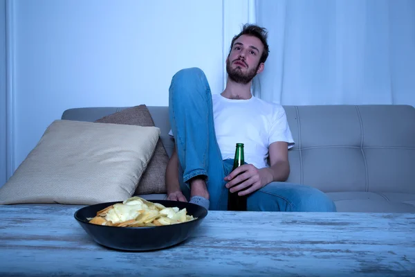 Jovem assistindo TV à noite com batatas fritas e cerveja — Fotografia de Stock