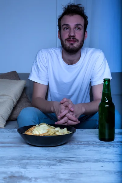 Молодой человек смотрит кино ночью с чипсами и пивом — стоковое фото