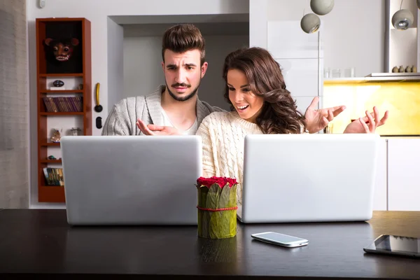 Casal jovem na frente de seus computadores portáteis em casa — Fotografia de Stock