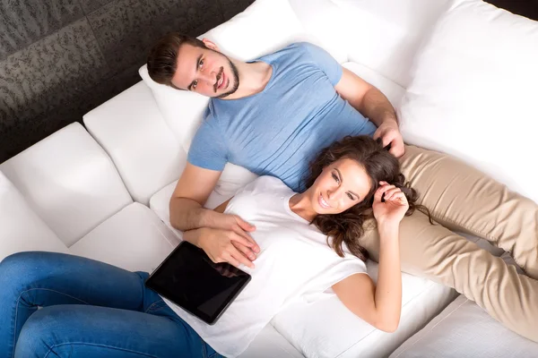 Νεαρό ζευγάρι που χρησιμοποιούν ένα Tablet PC μαζί στον καναπέ στο σπίτι — Φωτογραφία Αρχείου