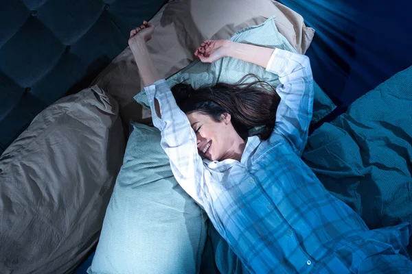 Uykulu genç kadın akşamları yatakta geriniyor. — Stok fotoğraf