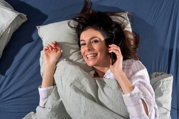 Een gelukkige jonge vrouw in bed die telefoneert — Stockfoto