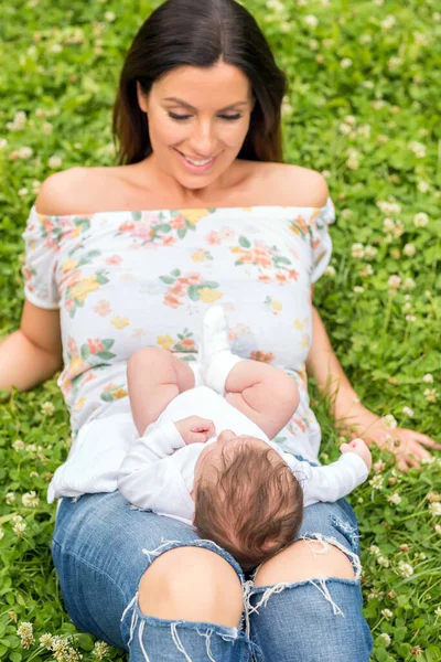 Une mère allongée sur l'herbe tandis que son bébé assis sur ses genoux — Photo