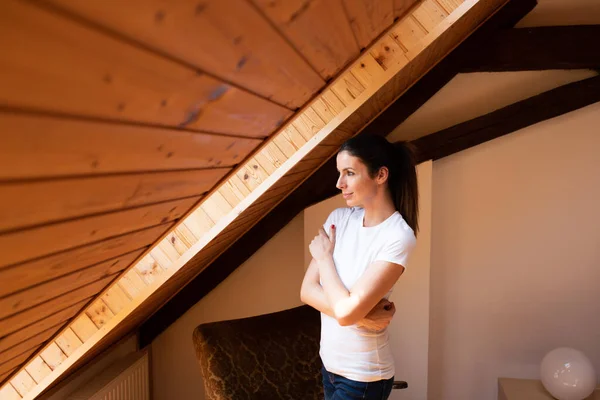 Una hermosa mujer de pie junto a la ventana de un ático — Foto de Stock