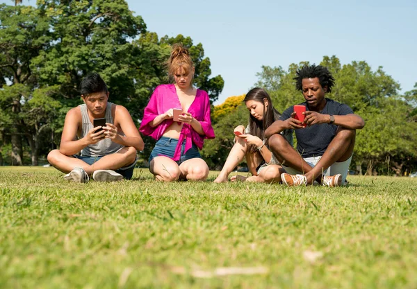 Barátok használják a telefonjukat a parkban. — Stock Fotó