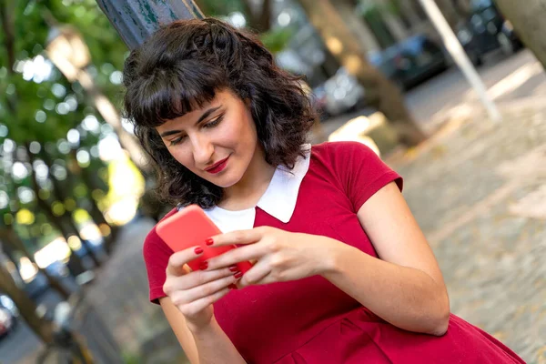 Μια γυναίκα σε ένα κόκκινο φόρεμα χρησιμοποιώντας το smartphone της Φωτογραφία Αρχείου