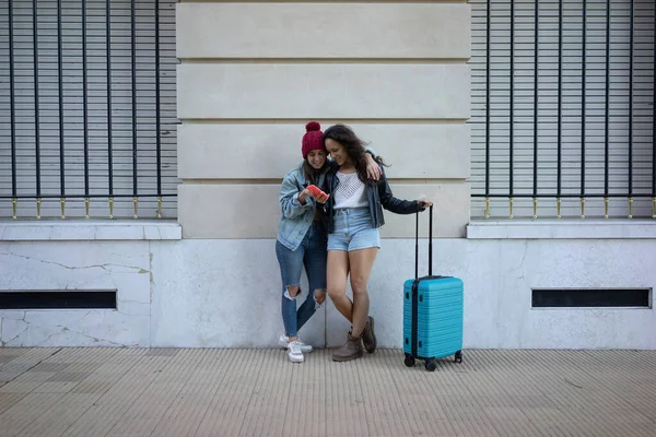 Lesbiennes debout dans la rue au mur avec une valise — Photo