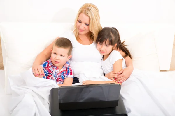 Madre con i suoi figli utilizzando un computer portatile a letto — Foto Stock