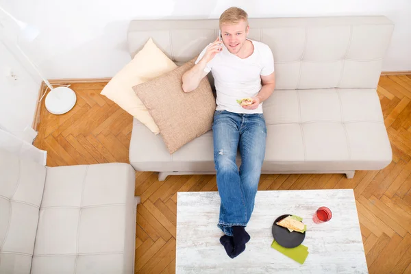 Joven con un sándwich en el sofá — Foto de Stock