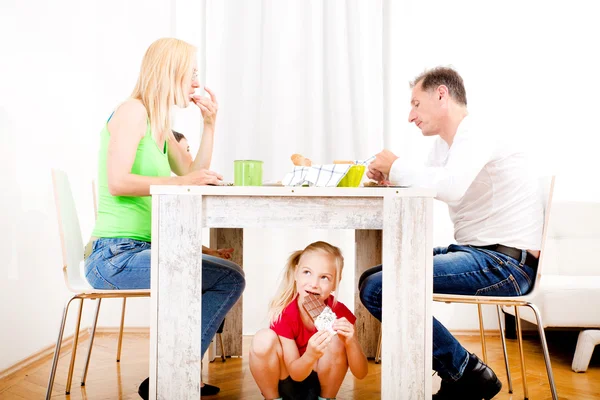 Ragazza mangiare cioccolato sotto la tavola — Foto Stock