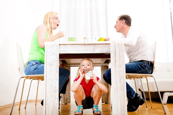 Ragazza mangiare cioccolato sotto la tavola — Foto Stock