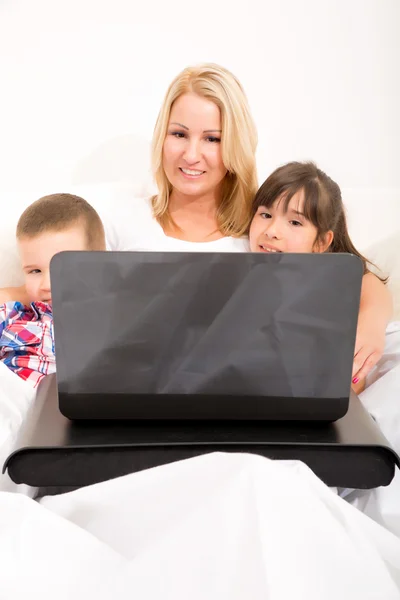 Madre con sus hijos usando un portátil en la cama — Foto de Stock