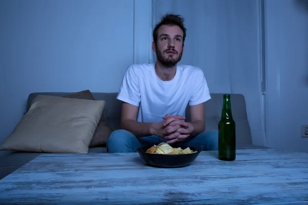 Young man watching TV at nighttime with chips and beer — Stock Photo, Image
