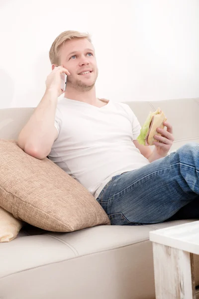 Joven con un sándwich en el sofá — Foto de Stock