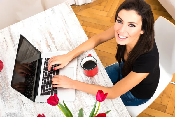 Jovem mulher bonita sorrindo ao usar um laptop em casa — Fotografia de Stock