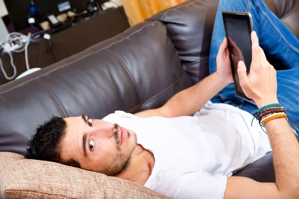 Jovem macho com tablet em um sofá — Fotografia de Stock