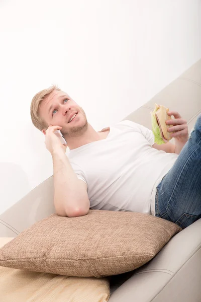 Молодой человек с бутербродом на диване — стоковое фото