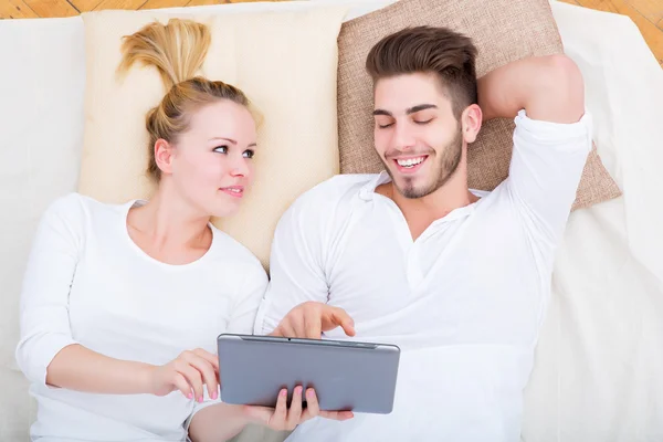 Jeune couple avec une tablette PC au lit — Photo