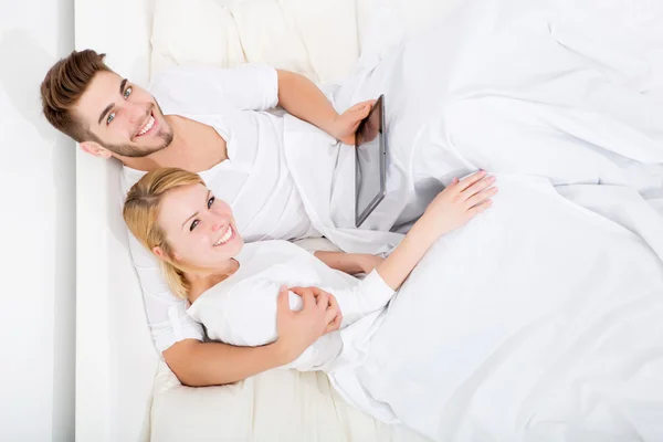 Jeune couple avec une tablette PC au lit — Photo