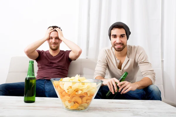 Dos amigos viendo apasionadamente la televisión con cerveza y patatas fritas — Foto de Stock