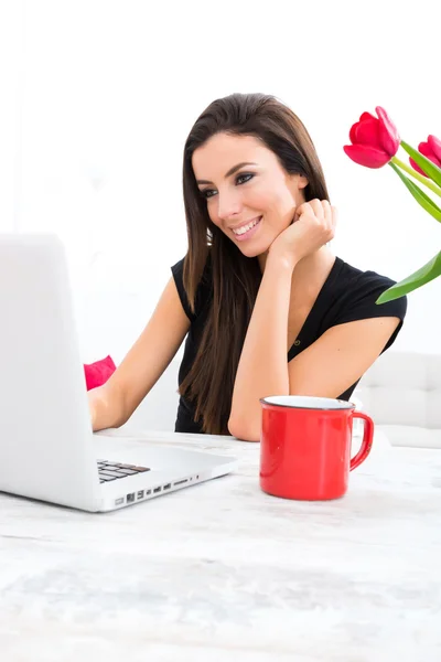 Jovem mulher bonita sorrindo ao usar um laptop em casa — Fotografia de Stock