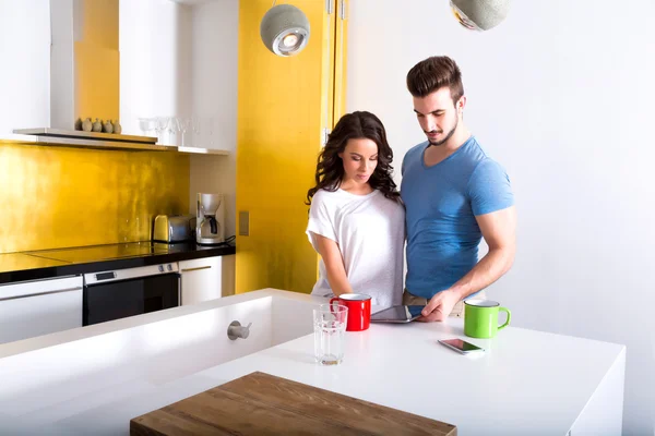 Casal jovem usando um Tablet PC na cozinha em casa — Fotografia de Stock