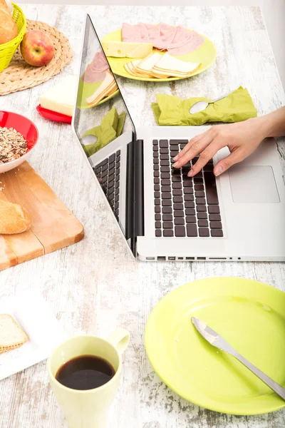 Jovem mulher tomando café da manhã ao usar um computador portátil — Fotografia de Stock