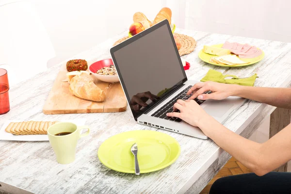 Mujer joven desayunando mientras usa una computadora portátil — Foto de Stock