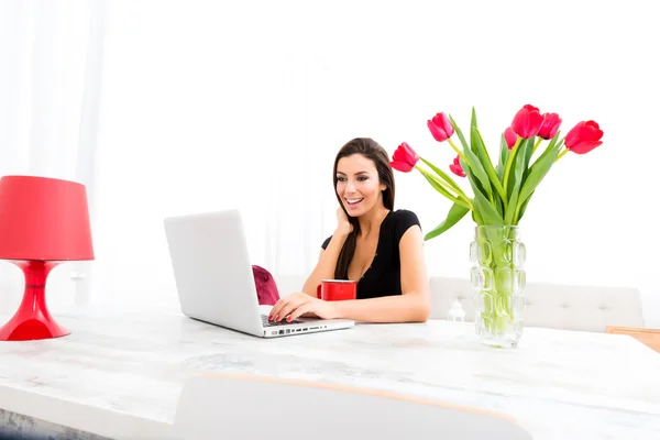Jovem mulher bonita sorrindo ao usar um laptop em casa — Fotografia de Stock