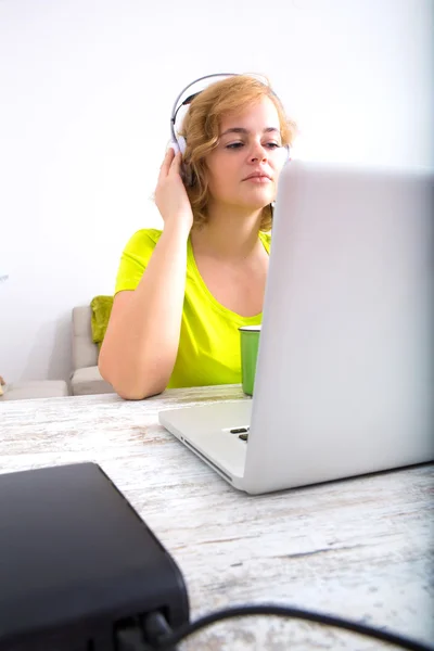 Ung vuxen kvinna med hörlurar framför en laptop — Stockfoto