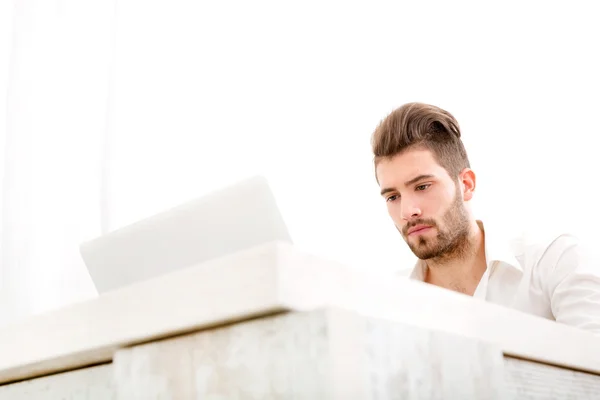 Varón joven en su casa con un ordenador portátil — Foto de Stock