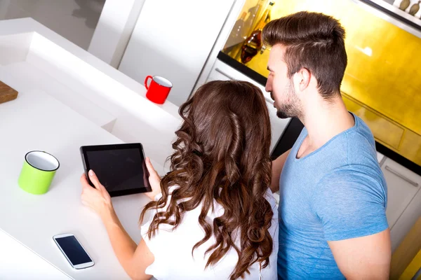 Casal jovem usando um Tablet PC na cozinha em casa — Fotografia de Stock