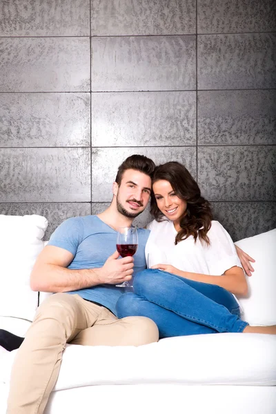 Krásný pár, kteří požívají sklenku vína na pohovce — Stock fotografie
