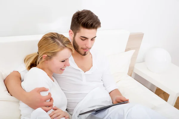 Jeune couple avec une tablette PC au lit — Photo