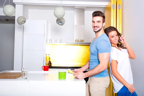 Young couple using their digital devices at home in the kitchen — Stock Photo, Image