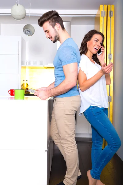 Mladý pár, pomocí jejich digitálních zařízení doma v kuchyni — Stock fotografie