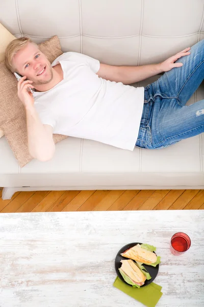 Jeune homme avec un sandwich sur le canapé — Photo