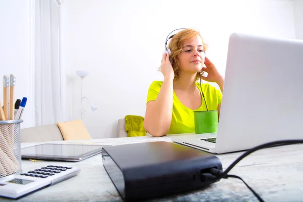 Bir dizüstü bilgisayar önünde kulaklıklarla genç yetişkin kadın — Stok fotoğraf