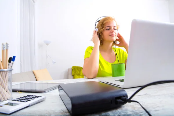 Ung vuxen kvinna med hörlurar framför en laptop — Stockfoto