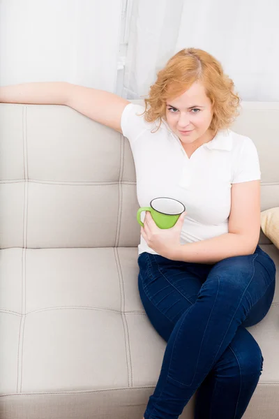 Jonge vrouw met een kopje koffie op de Bank — Stockfoto