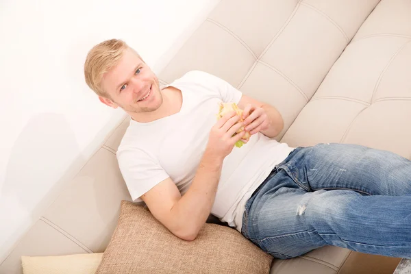 Jeune homme mangeant un sandwich à la maison — Photo