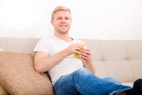 Joven comiendo un sándwich en casa — Foto de Stock