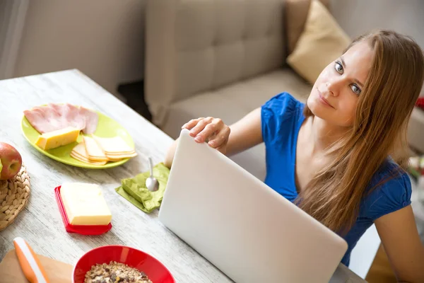 Ung kvinna äter frukost medan du använder en bärbar dator — Stockfoto