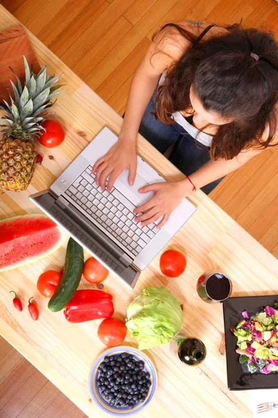 Mujer usando un ordenador portátil mientras cocina — Foto de Stock