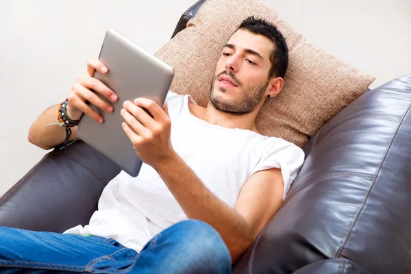 Joven macho con la tableta en un sofá — Foto de Stock