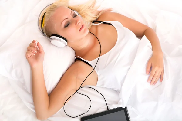 Chica rubia acostada en la cama escuchando música — Foto de Stock
